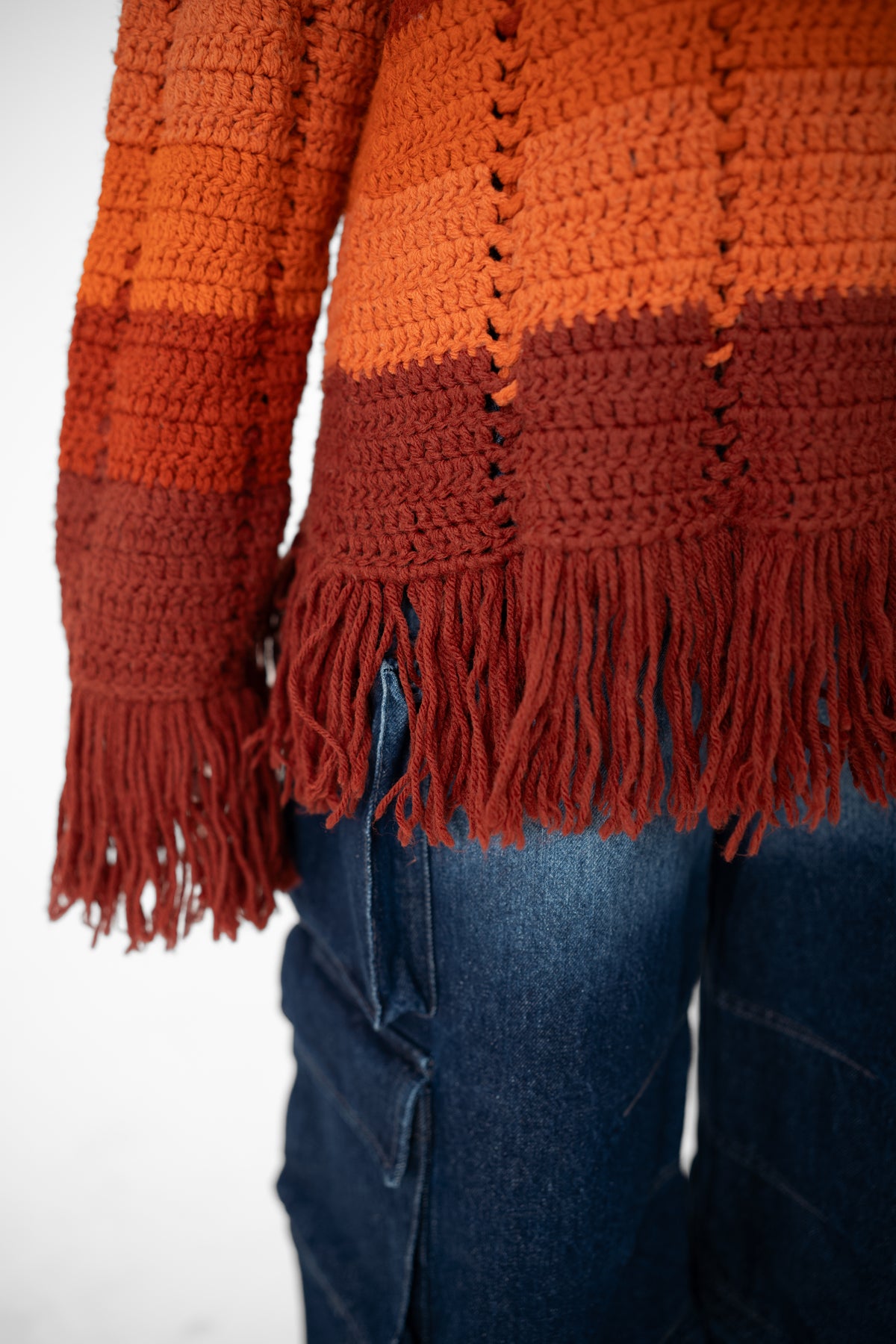 Close-up of the Afterglow hoodie's hand-crocheted rust and orange stripes and fringed hem