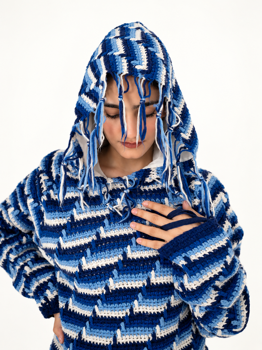 Close-up of the Blue Frequency crochet hood with knotted blue and ivory tassel fringe and thumb-loop sleeve