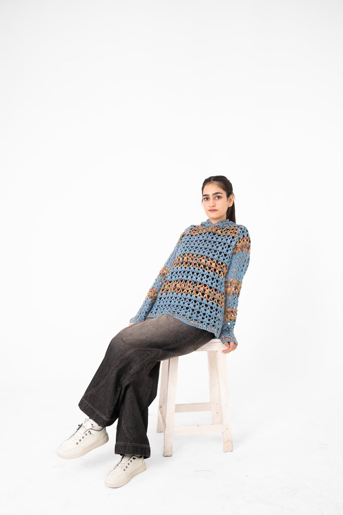Mosaic Mood dusty blue multicolour crochet hoodie, model seated on a white stool