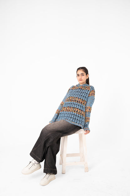 Mosaic Mood dusty blue multicolour crochet hoodie, model seated on a white stool