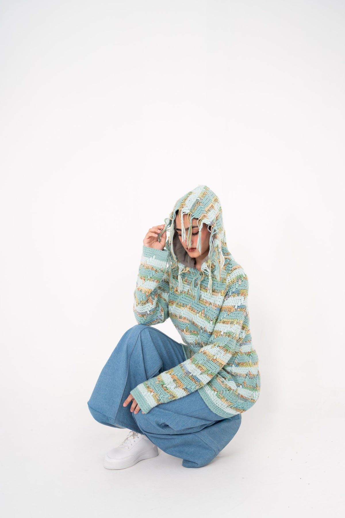 Pastel Static fringed crochet hoodie with hood up, model crouching