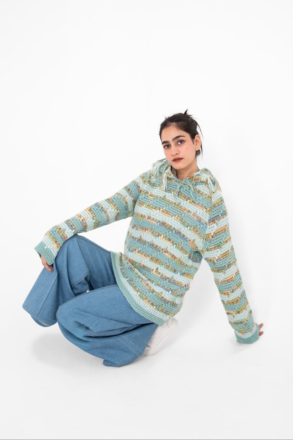 Pastel Static mint multicolour crochet hoodie, model seated in light blue wide-leg jeans