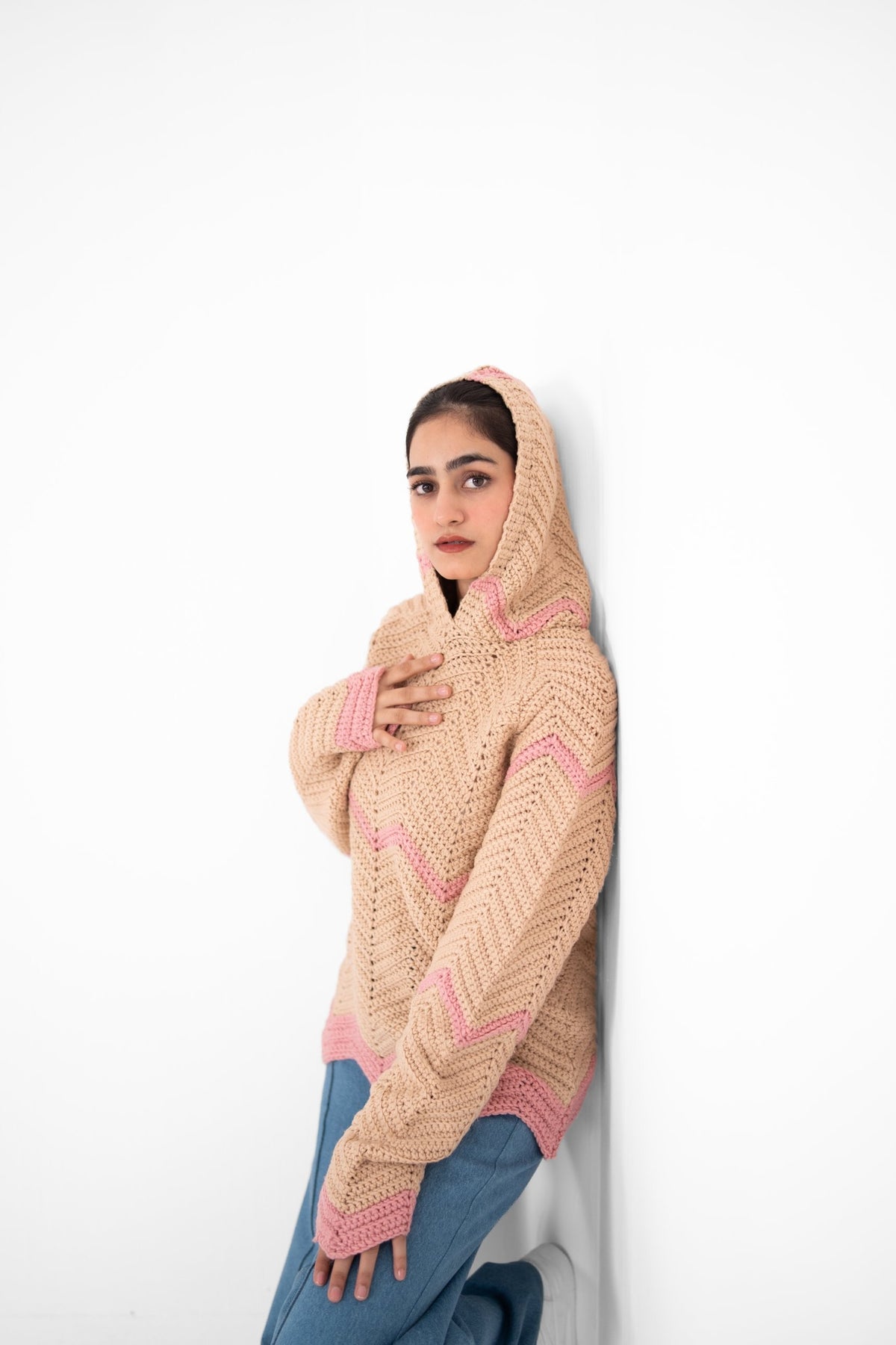Model leaning on a wall in Pink Plot Twist handmade crochet hoodie with hood up – POSHERI
