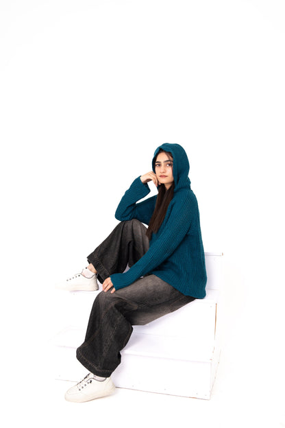 Teal Deal crochet hoodie with hood up, model seated on white steps